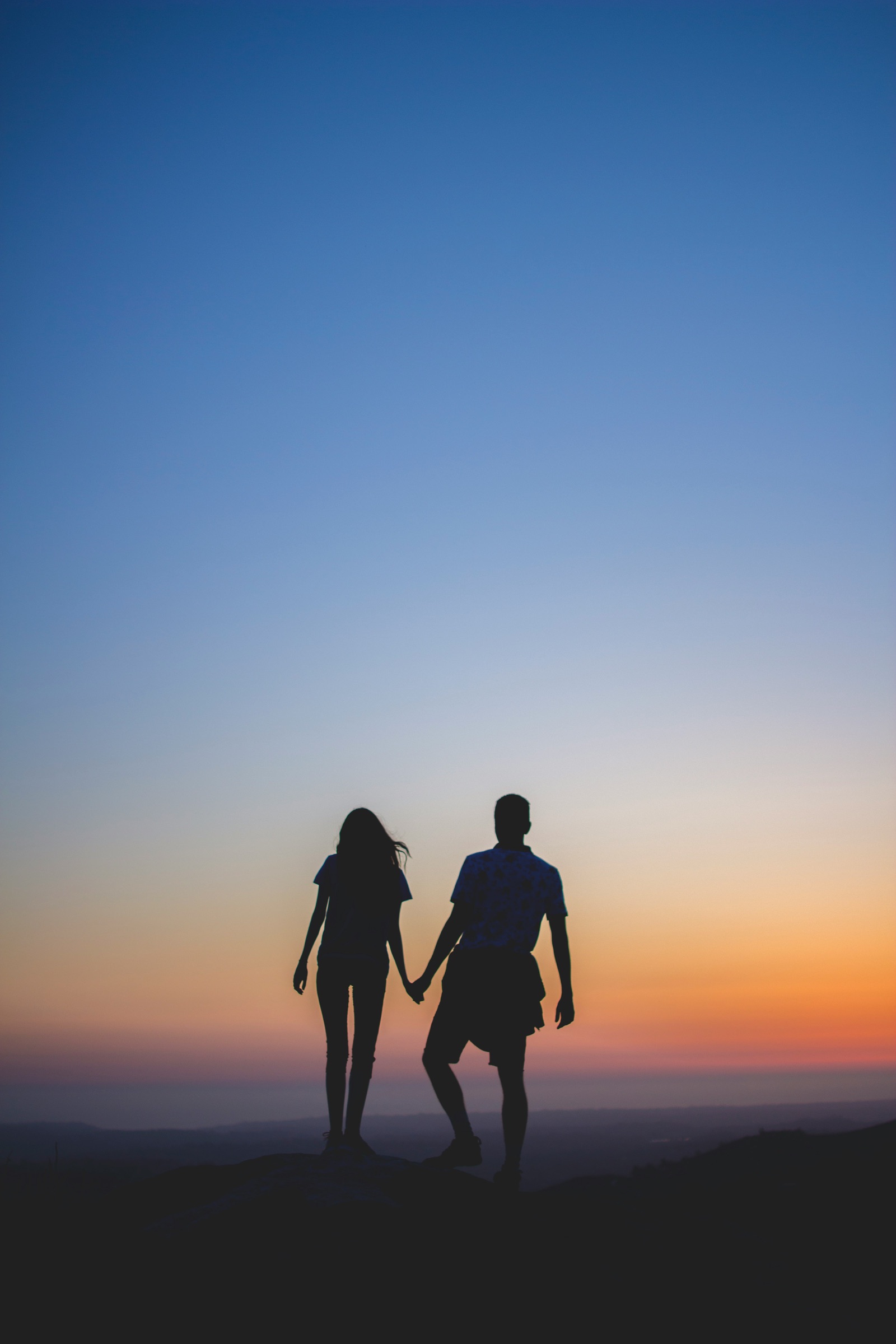 Un couple main dans la main, en silhouette, face au coucher du soleil.